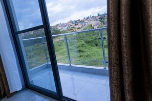 A balcony with a metal railing, a glass door, and a view of a green landscape with houses.