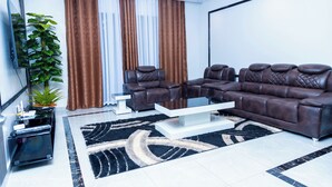 A modern living room with a sectional sofa, a coffee table, and a large plant. - Exclusive 4BR/3BA Penthouse Lux Apartment + Rooftop @ BBB Nation Oasis in Kigali (Kigali)