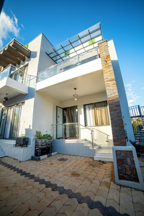 A modern two-story house with a balcony, large windows, and a paved driveway.