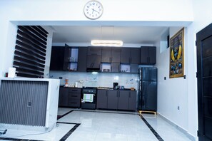 Une cuisine moderne avec des meubles de couleur sombre, un four encastré et une grande horloge au mur.