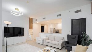 Un salon moderne avec un téléviseur à écran plat, des canapés blancs, une table basse et un fauteuil foncé.