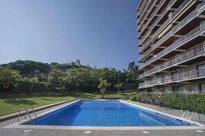 Une piscine à l’eau d’un bleu limpide, entourée d’une pelouse bien entretenue et d’un immeuble à plusieurs étages doté de balcons.