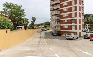 Een meerlaags woongebouw met balkons, een parkeerplaats met meerdere auto's, en een gele muur aan één kant.