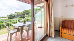 Ein Balkon mit Tisch und Stühlen, einer Holz-Sofaecke und Blick auf Grünflächen und Gebäude.