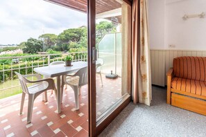 Ein Balkon mit Tisch und Stühlen, einer Holz-Sofaecke und Blick auf Grünflächen und Gebäude.