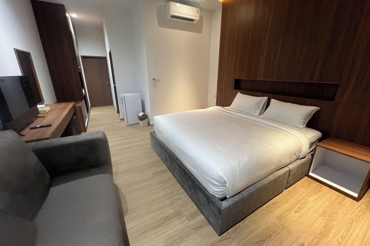 A modern hotel room with a large bed, a desk, a chair, and a small kitchenette.