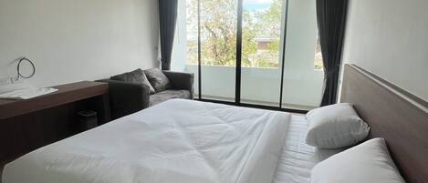 A hotel room with a large bed, a desk, and a view of the outdoors through a sliding door.