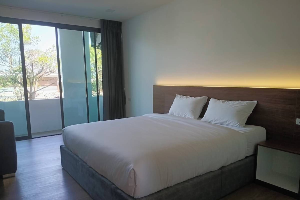 A modern hotel room with a large bed, a nightstand, and a view through a sliding glass door.