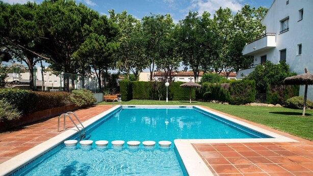 A rectangular swimming pool with a tiled deck, surrounded by well-maintained hedges and trees.