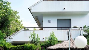 A modern white building with a flat roof, a small window, and a thatched structure nearby.