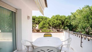 A balcony with a white table and chairs, a glass door, and a view of trees and buildings.