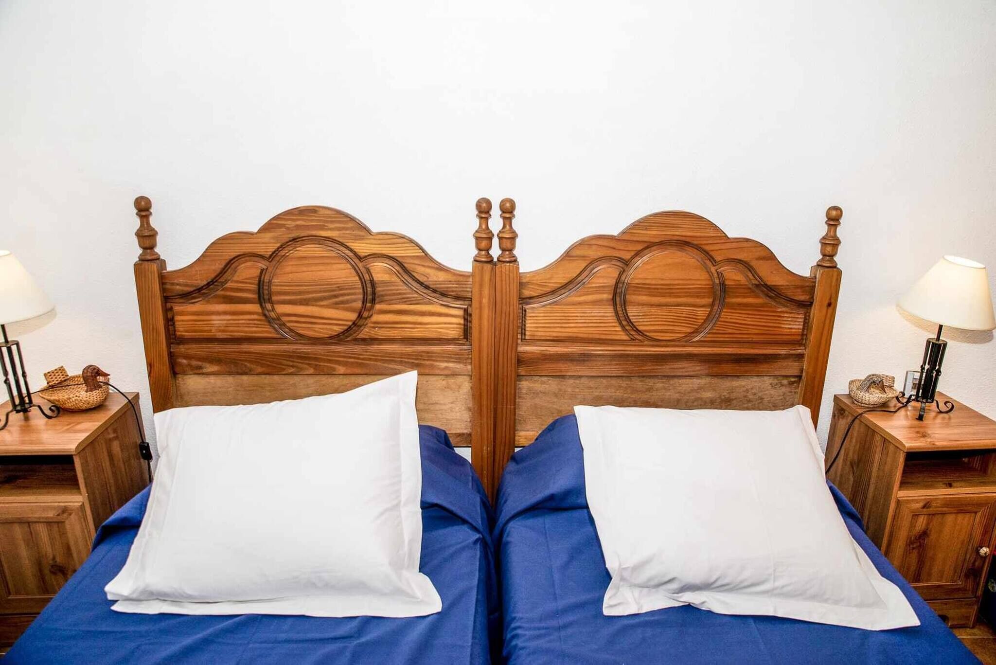 Un lit double avec une tête de lit en bois, deux tables de chevet avec des lampes et une couvre-lit bleue.