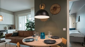 A modern kitchen with white cabinets, a dining area with a round table, and a living room with a brown sofa. - Balcony | Free Parking | 24h Shop (Helsinki)