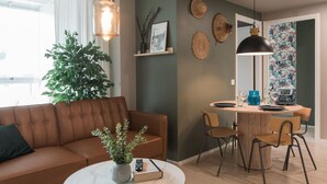 A modern living room with a brown leather sofa, a dining table with chairs, a potted plant, and a large mirror. - Balcony | Free Parking | 24h Shop (Helsinki)