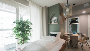 A modern hotel room with a bed, a dining table, chairs, a potted plant, and a large window. - Balcony | Free Parking | 24h Shop (Helsinki)