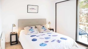 Ein Schlafzimmer mit einem Bett, zwei Nachttischen, einem gerahmten Bild an der Wand und Blick ins Freie durch ein großes Fenster.