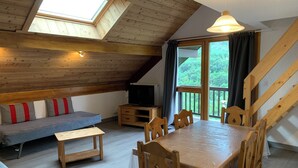 A cozy loft-style room with a wooden ceiling, a dining table with chairs, a sofa with cushions, a TV, and a large window with curtains. - 4-person apartment in Pelvoux! 67m2, mountain view Résidence Le Glacier Blanc (Vallouise-Pelvoux)