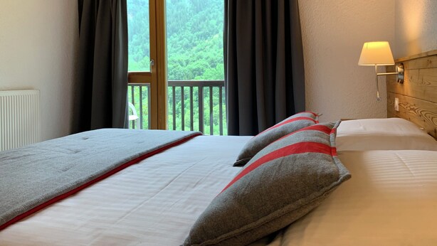 A hotel room with two beds, a view of greenery through the window, and a bedside lamp. - 4-person apartment in Pelvoux! 67m2, mountain view Résidence Le Glacier Blanc (Vallouise-Pelvoux)