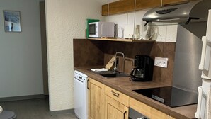 A compact kitchen with wooden cabinets, a built-in oven, a microwave, and a coffee maker. - 4-person apartment in Pelvoux! 67m2, mountain view Résidence Le Glacier Blanc (Vallouise-Pelvoux)