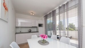 A modern kitchen with white cabinets, a microwave, and a dining area with a white table and chairs. - Villa Star 1 (Novalja)