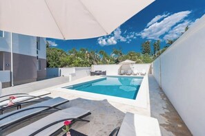 A modern outdoor pool area with a clear blue sky, a white umbrella, and lounge chairs. - Villa Star 1 (Novalja)