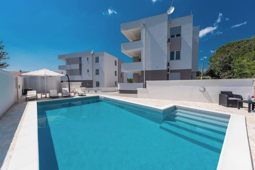 A modern building with a swimming pool, outdoor seating, and a clear sky.