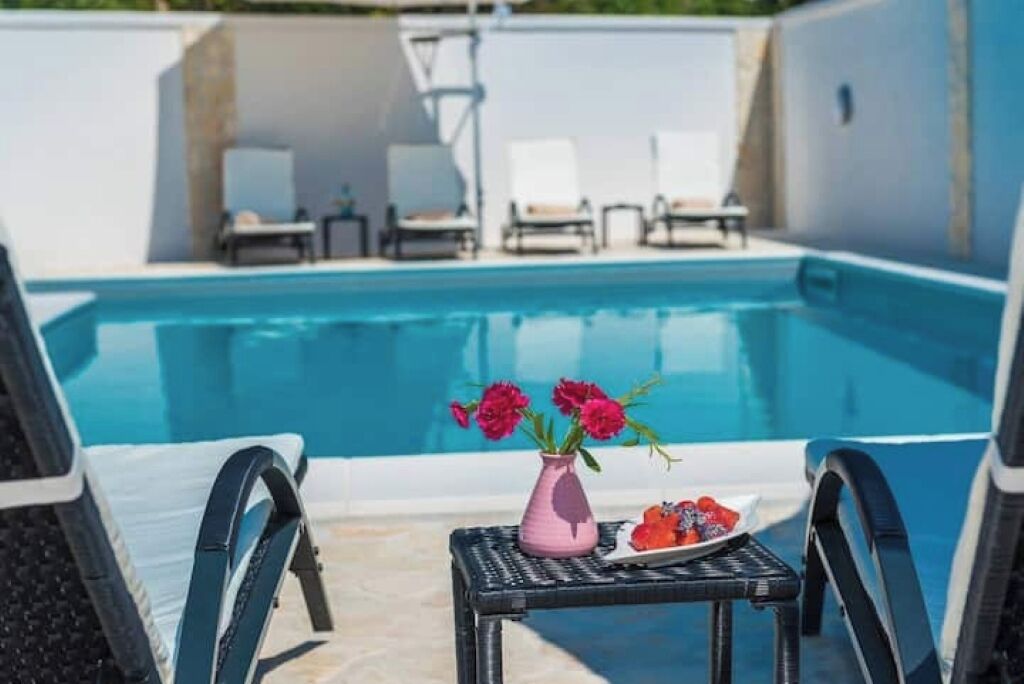 Un espace aménagé au bord de la piscine, avec des chaises longues et une petite table agrémentée d’un vase de fleurs et d’une assiette de fruits.