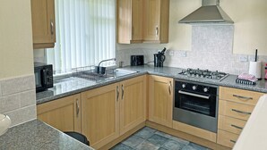 Une cuisine compacte avec des meubles en bois, un four encastré, une cuisinière à gaz et une fenêtre équipée de stores.