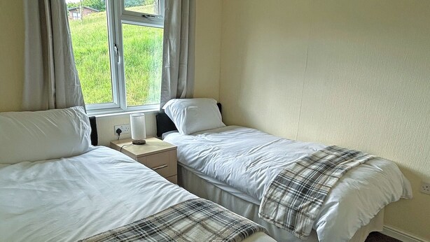 A room with two beds, a nightstand, a lamp, and a window with curtains.