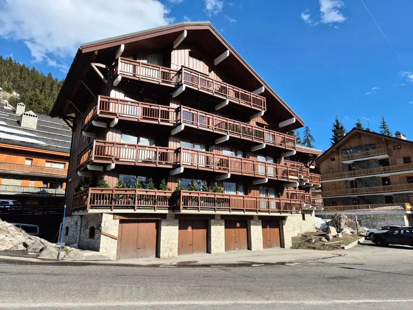 A multi-story wooden building with balconies, stone walls, and a parking area.