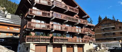 A multi-story wooden building with balconies, stone walls, and a parking area.