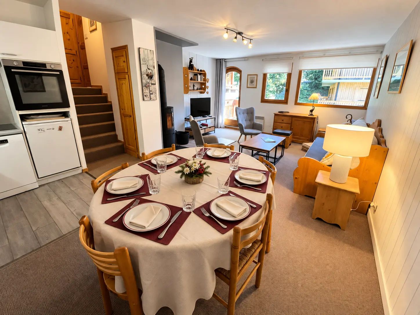 A dining area with a round table set for four, a kitchen with modern appliances, and a cozy living space with a sofa and lamp.