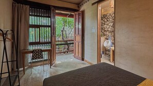 A room with a bed, a chair, a table, a window with a view of trees, and a stone wall.