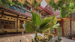 A courtyard with a central palm tree, a stone wall, and a building with balconies and windows.