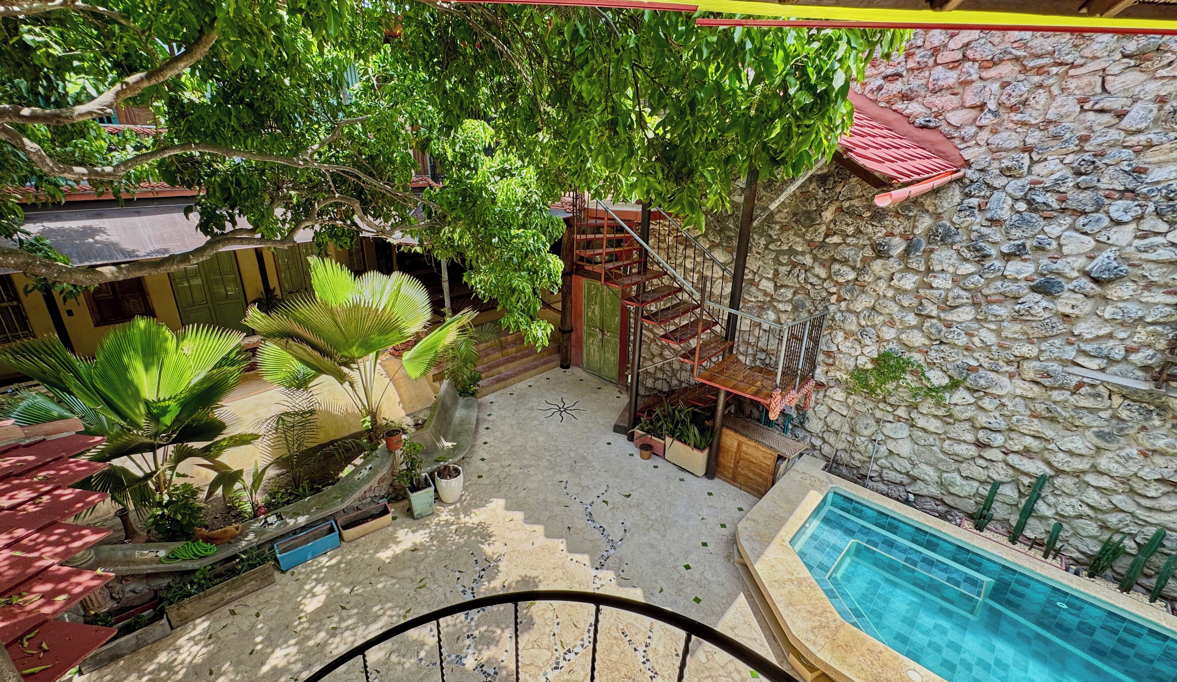 A pool area with a stone wall, a spiral staircase, and various plants.