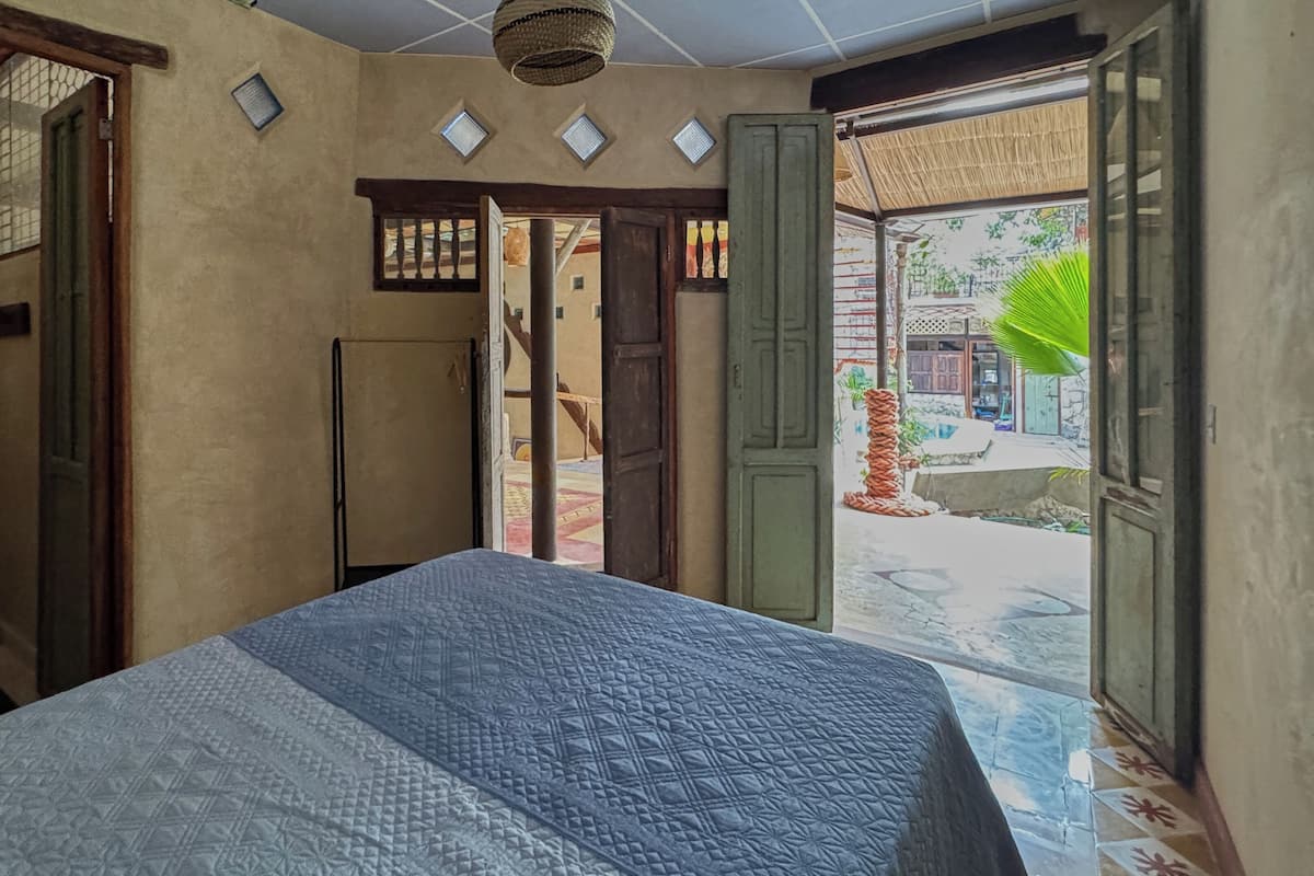 Una habitación con una cama, una puerta que da al exterior y un ventanal pequeño.