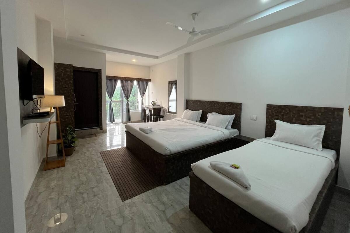 A hotel room with two beds, a desk, a chair, a TV, and a view of the outdoors.