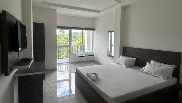 Een moderne slaapkamer met een groot bed, een televisie en een balkon met stoelen.