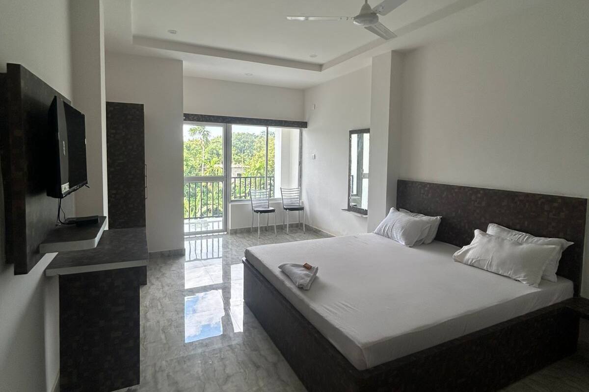 A modern bedroom with a large bed, a TV, and a balcony with chairs.