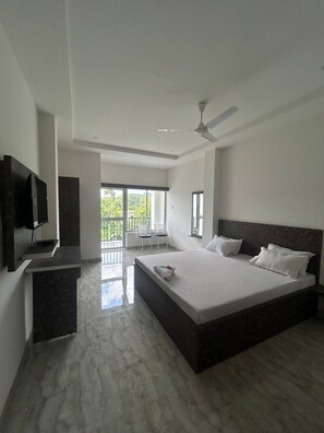 A modern bedroom with a large bed, a TV, and a balcony with chairs. - Sneha Bhawan Kaziranga (Bokakhat)