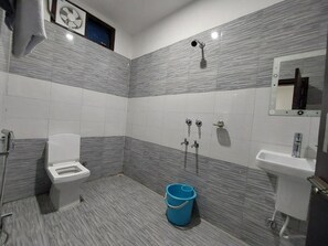 Een badkamer met een toilet, bidet, wastafel en een blauwe emmer.