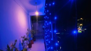 Een balkon met blauwe lichtslingers, potplanten en een uitzicht op de stad 's nachts.