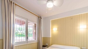 A hotel room with a bed, a ceiling fan, a window with curtains, and a wall-mounted light. - 38.10 S'AgaróCaleta So 206i  Apartment with terrace and views (Sant Feliu de Guixols)