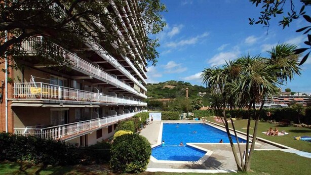 A hotel with a swimming pool, a multi-story building with balconies, and a lush green landscape. - 38.10 S'AgaróCaleta So 206i  Apartment with terrace and views (Sant Feliu de Guixols)