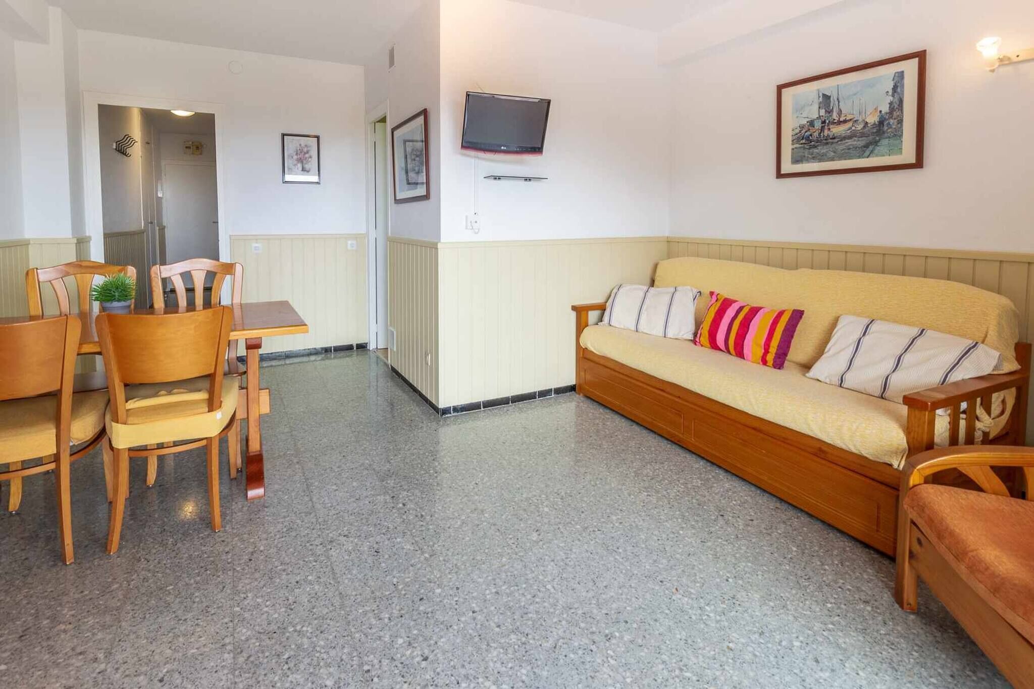 Ein gemütliches Wohnzimmer mit einer Couch, Sesseln, einem Esstisch und einem an der Wand befestigten Fernseher.