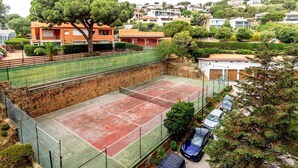 A tennis court surrounded by residential buildings, a large tree, and parked cars. - 38.10 S'AgaróCaleta So 206i  Apartment with terrace and views (Sant Feliu de Guixols)