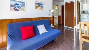 Ein Zimmer mit einem blauen Sofa, zwei Kissen, einer Holztür, einer weißen Wand und einem gerahmten Gemälde.