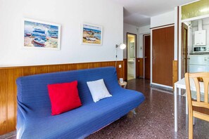Una habitación con un sofá azul, dos almohadas, una puerta de madera, una pared blanca y un cuadro enmarcado.