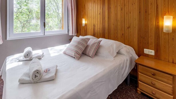 Ein Schlafzimmer mit einer Holzwand, einem Bett mit weißer Bettwäsche, zwei Kissen und zwei gerollten Handtüchern auf dem Bett.