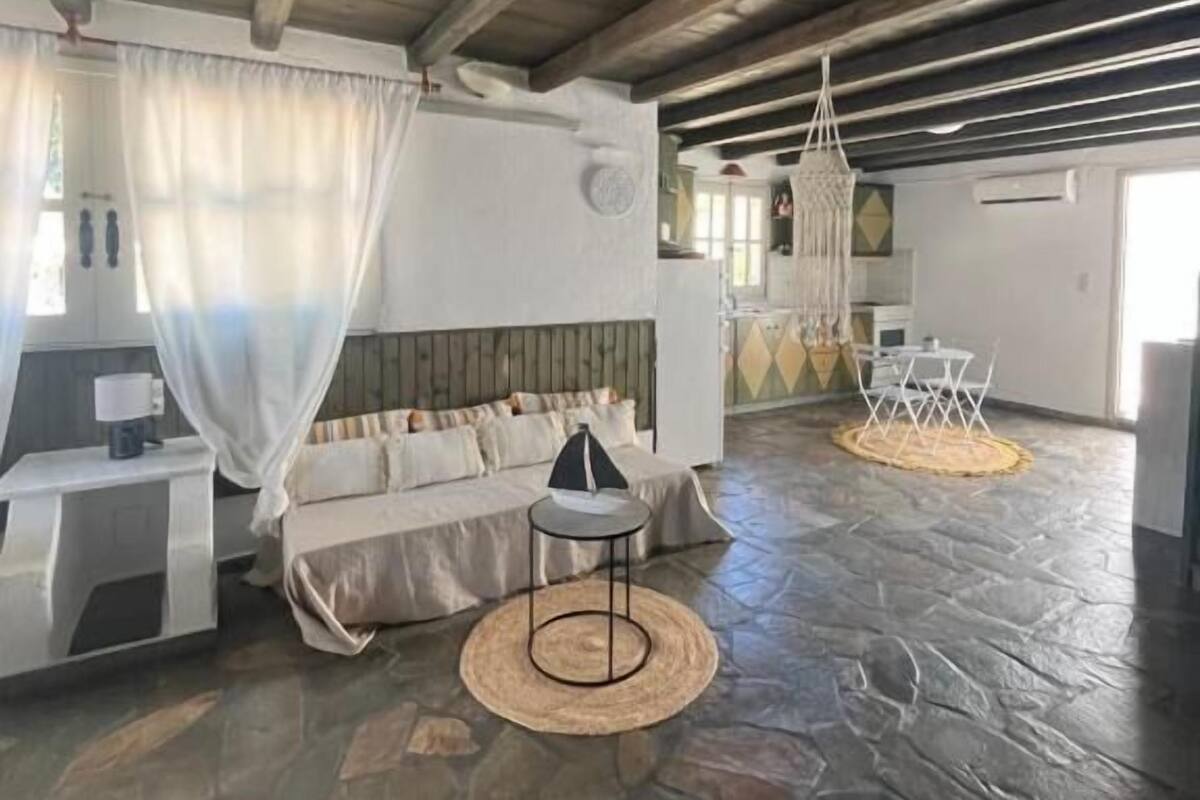 Una stanza spaziosa con pavimento in pietra, soffitto in legno, un divano, un tavolino e un lampadario.